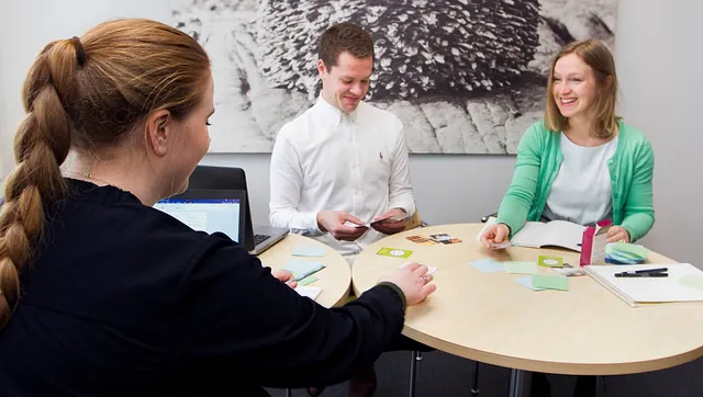 Tre trainees sittende ved et rundbord på kontoret